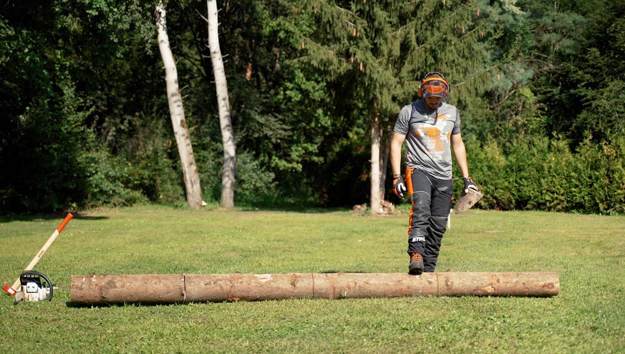 Persoon draait met de voet een boomstam om, om brandhout te zagen