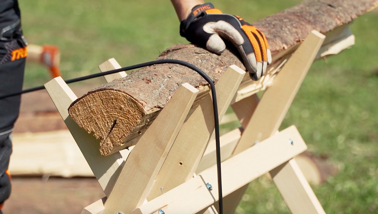 Een stuk hout wordt met spanrubber op een zaagblok vastgezet om het tot brandhout te zagen.
