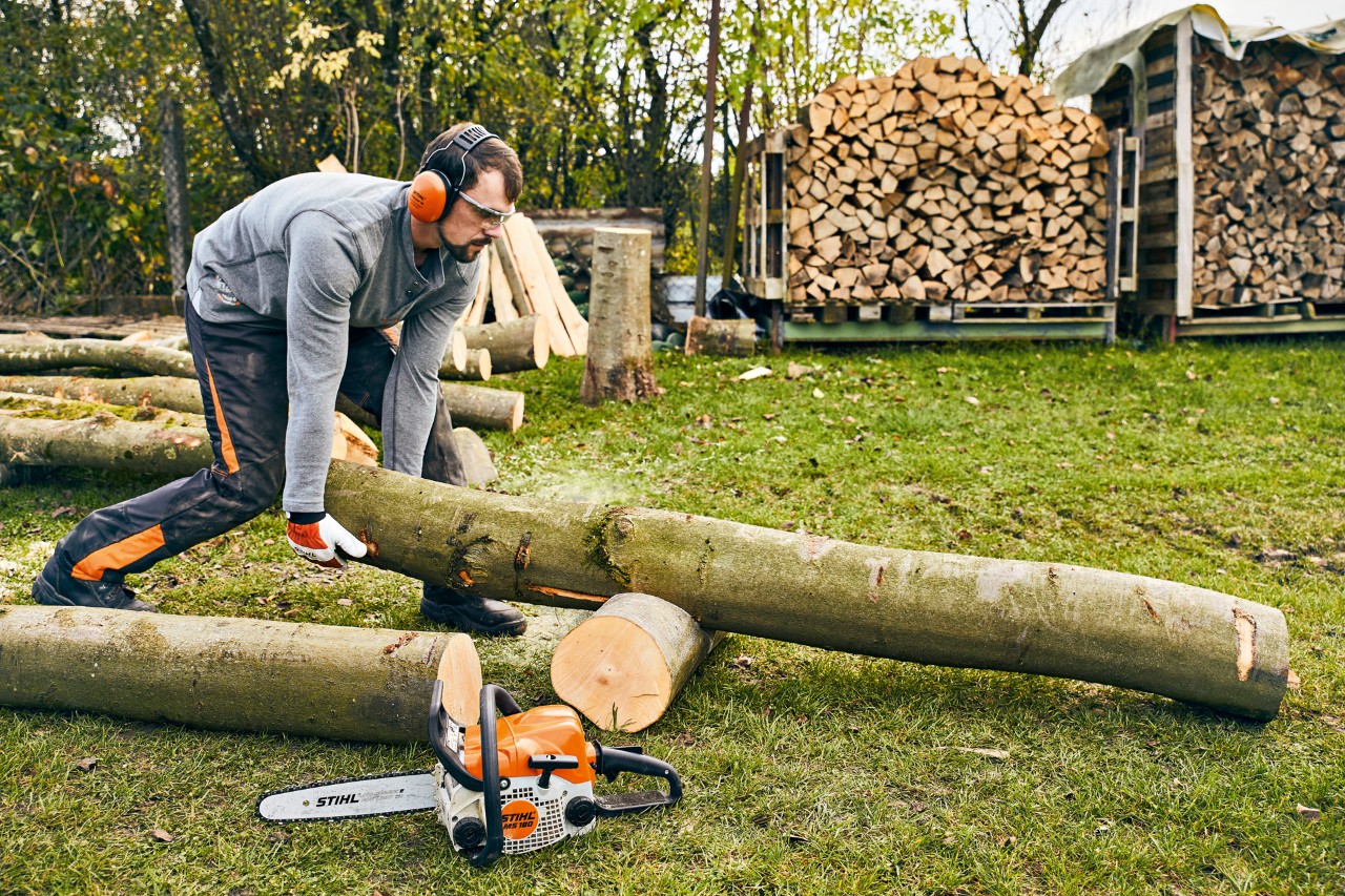 De boomstam wordt op de steun geplaatst om hem op lengte te zagen. Ernaast ligt een STIHL MS 180 benzinekettingzaag.