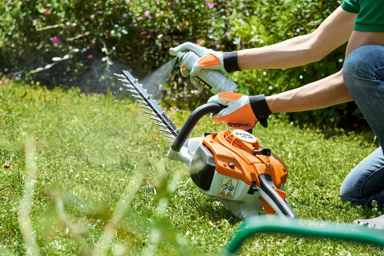  STIHL benzineheggenschaar HS 82 T wordt op groen gazon ingespoten om hem schoon te maken
