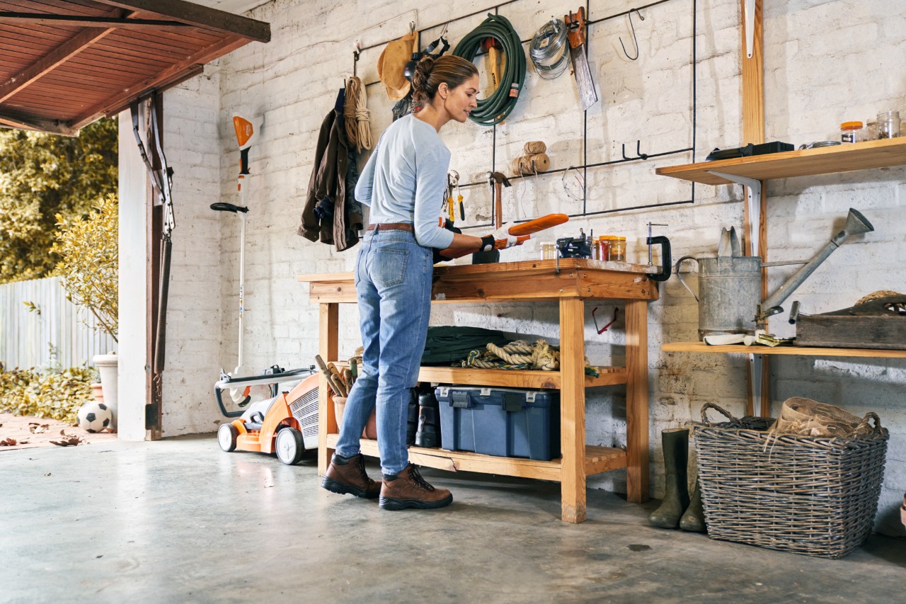 Vrouw met veiligheidshandschoenen bij het onderhoud van een STIHL HSA 56 accuheggenschaar op een werkbank
