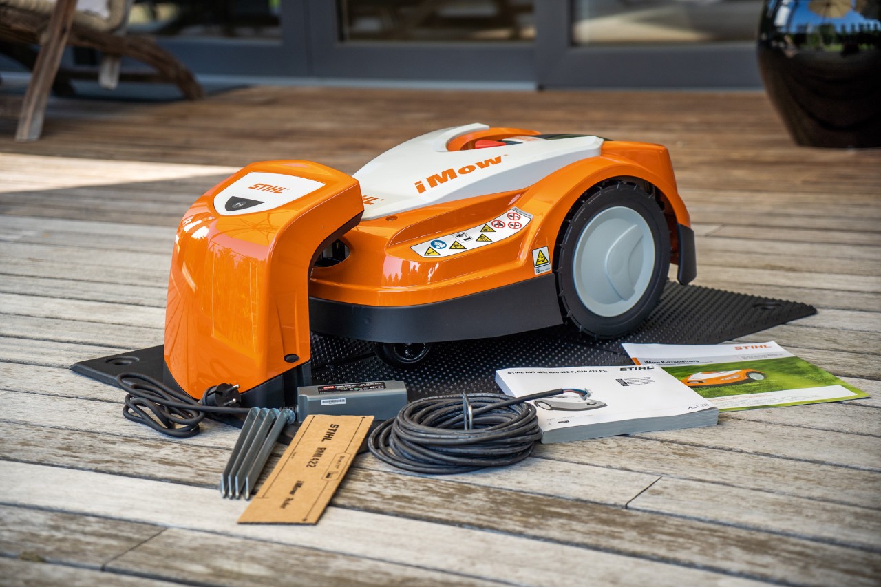 STIHL iMOW® robotmaaier 422 op houten terras met kabel en gebruiksaanwijzing vóór de installatie