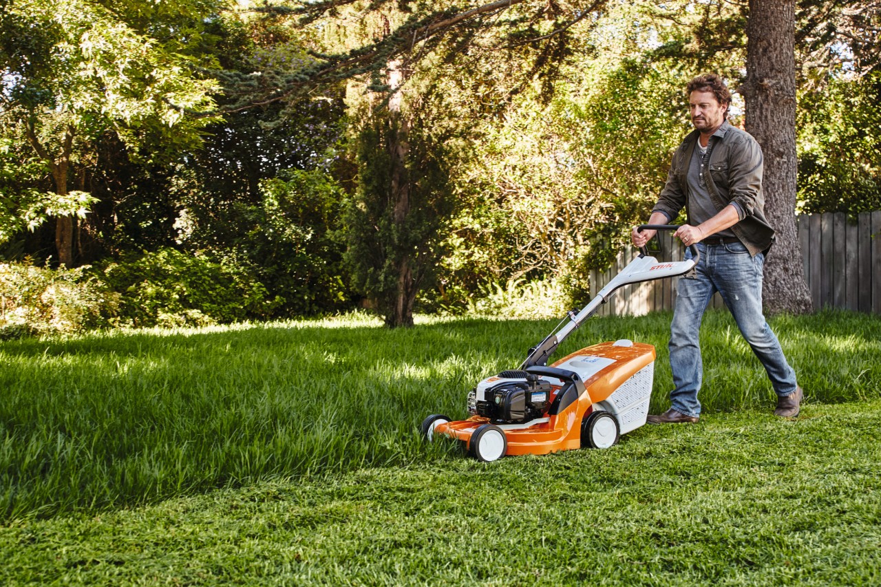 Een man maait het gras in een tuin met een STIHL grasmaaier 