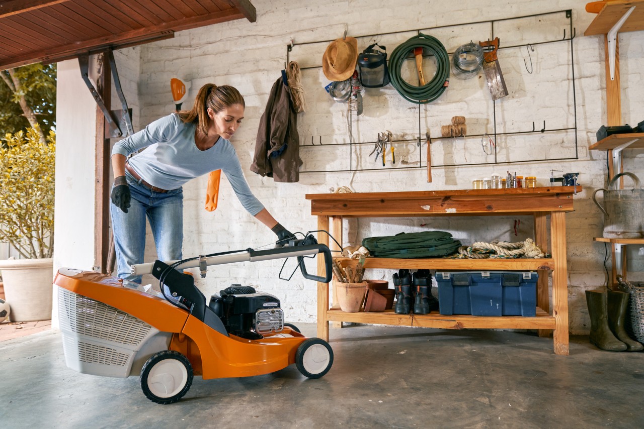 Vrouw maakt de STIHL RM 448 TC benzinegrasmaaier winterklaar in de garage en bergt hem op