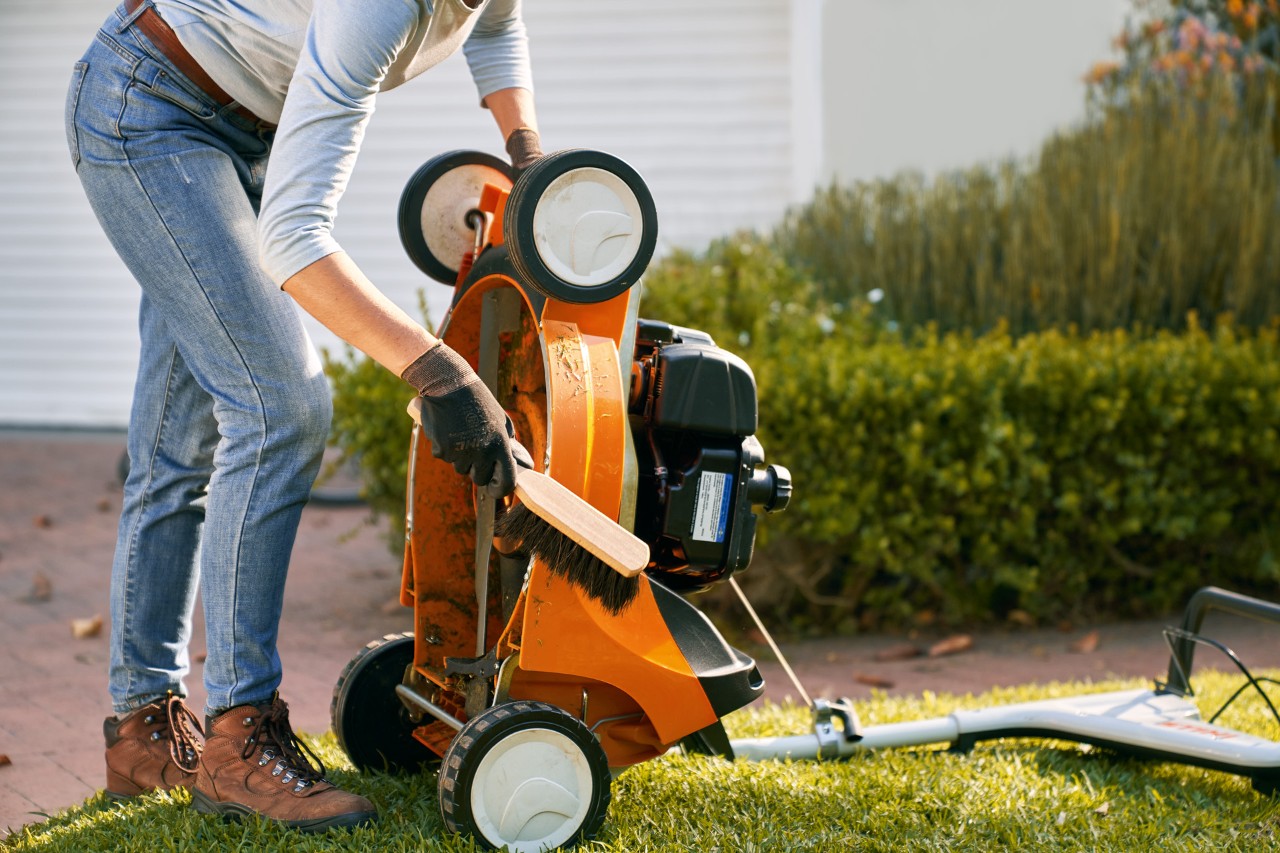 Een opstaande STIHL RM 448 T-C benzinegrasmaaier wordt gereinigd met een handborstel