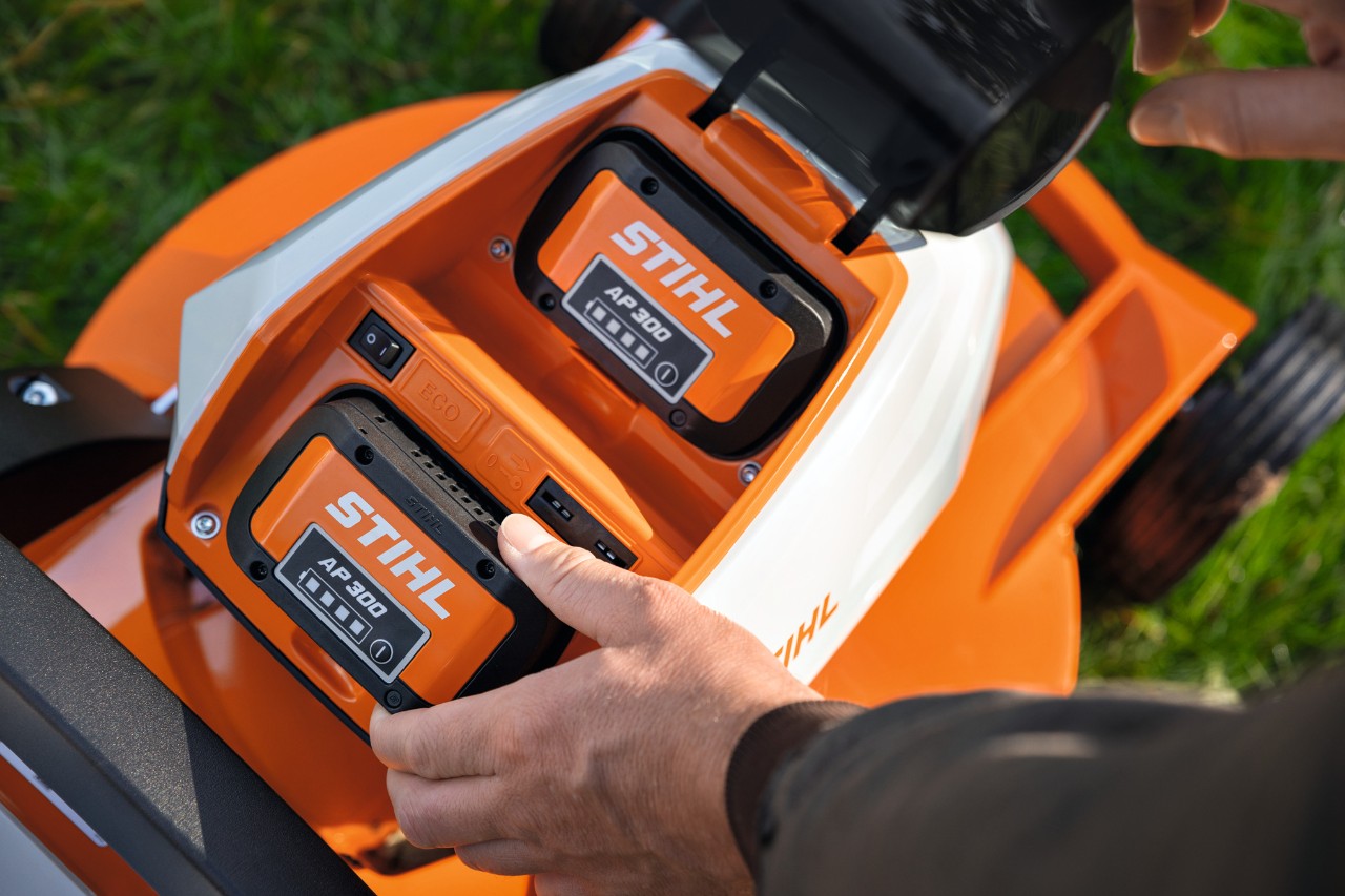 Iemand plaatst de volledig opgeladen STIHL AP 300 accu in een grasmaaier
