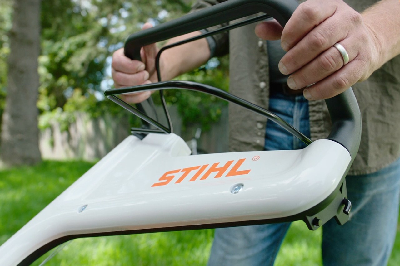 Iemand drukt de motorstopbeugel van een STIHL grasmaaier in