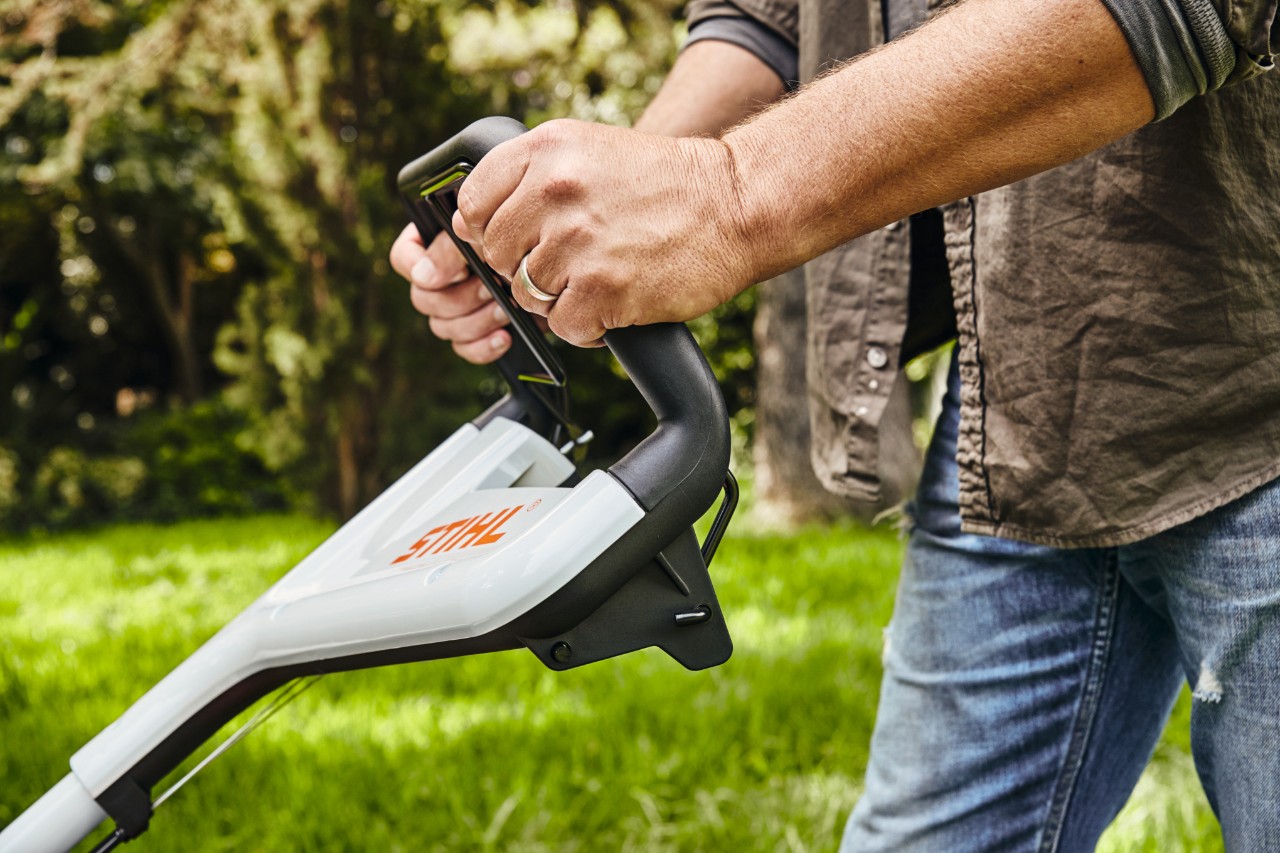 Een man houdt de STIHL RM 448 TC benzinegrasmaaier aan de duwstang vast om het gras te maaien