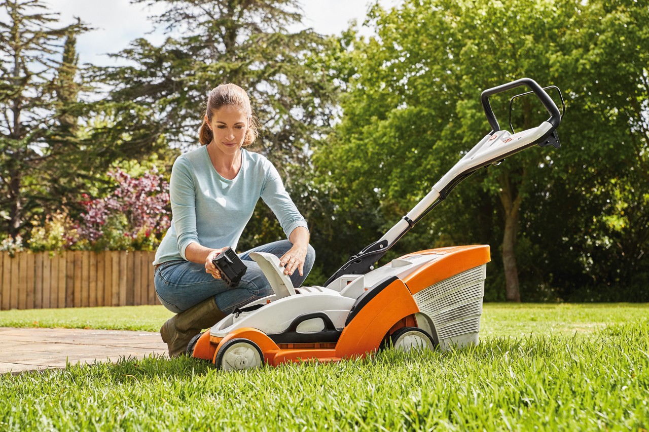 Een vrouw knielt naast een STIHL RMA 339C accugrasmaaier en verwijdert de accu.