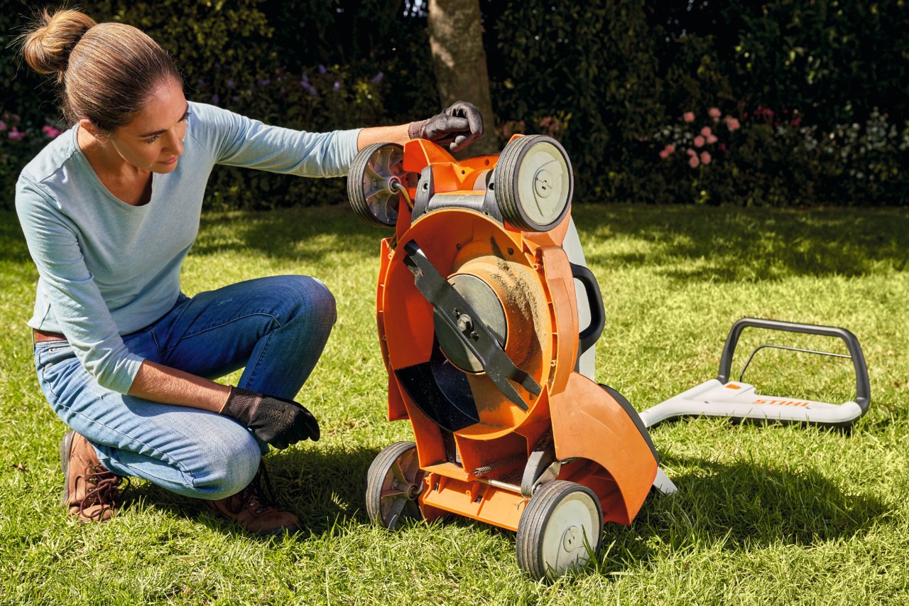 A woman kneeling checks the mower deck of STIHL RMA 339 C