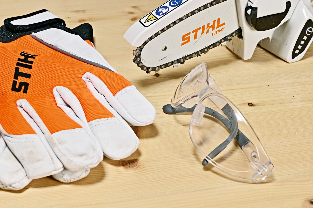 STIHL GTA 26 accusnoeizaag, STIHL veiligheidshandschoenen en -bril op een houten bank