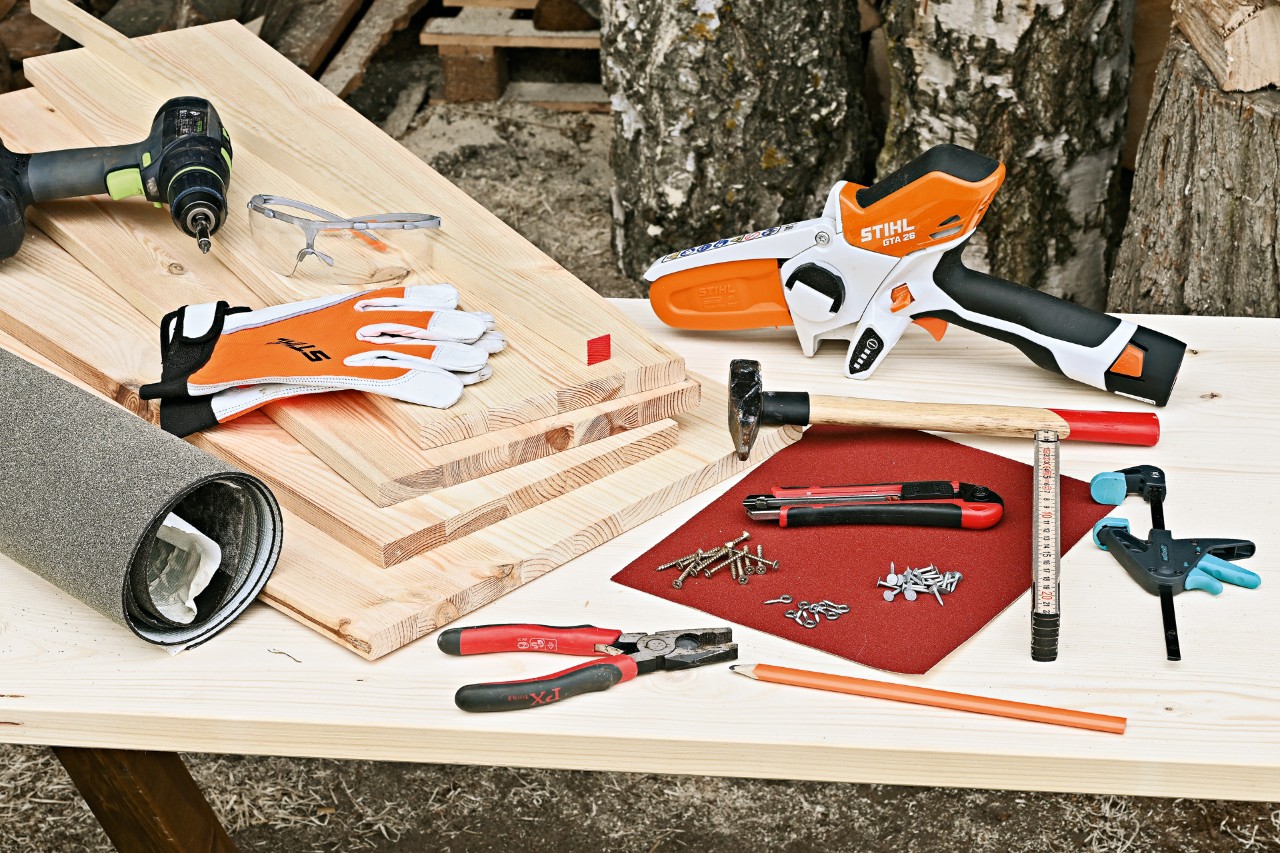 Doe-het-zelf-egelhuisje en materialen: STIHL GTA 26 accusnoeizaag, houten panelen, hamer, spijkers en ander gereedschap