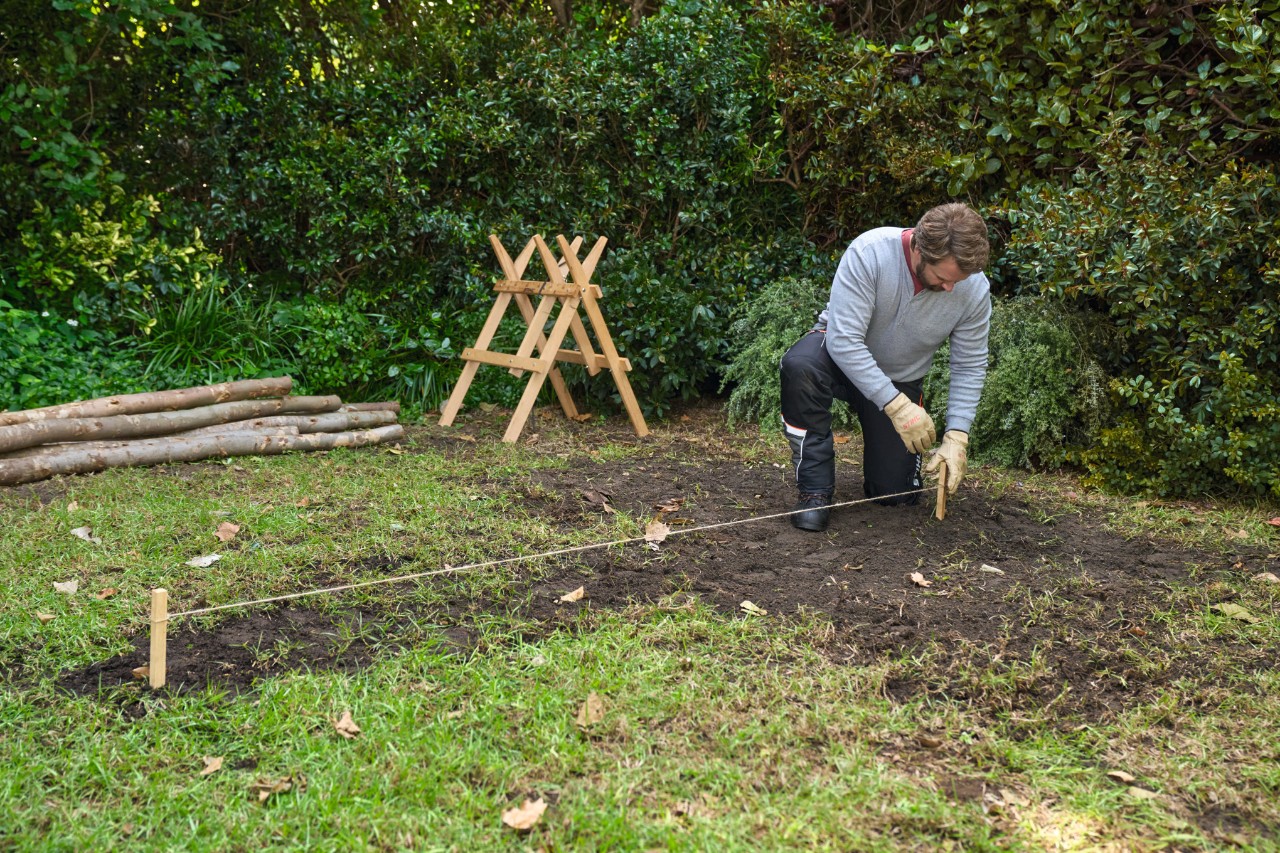 Een man steekt houten paaltjes die met een henneptouw met elkaar zijn verbonden in de grond om het oppervlak af te grenzen