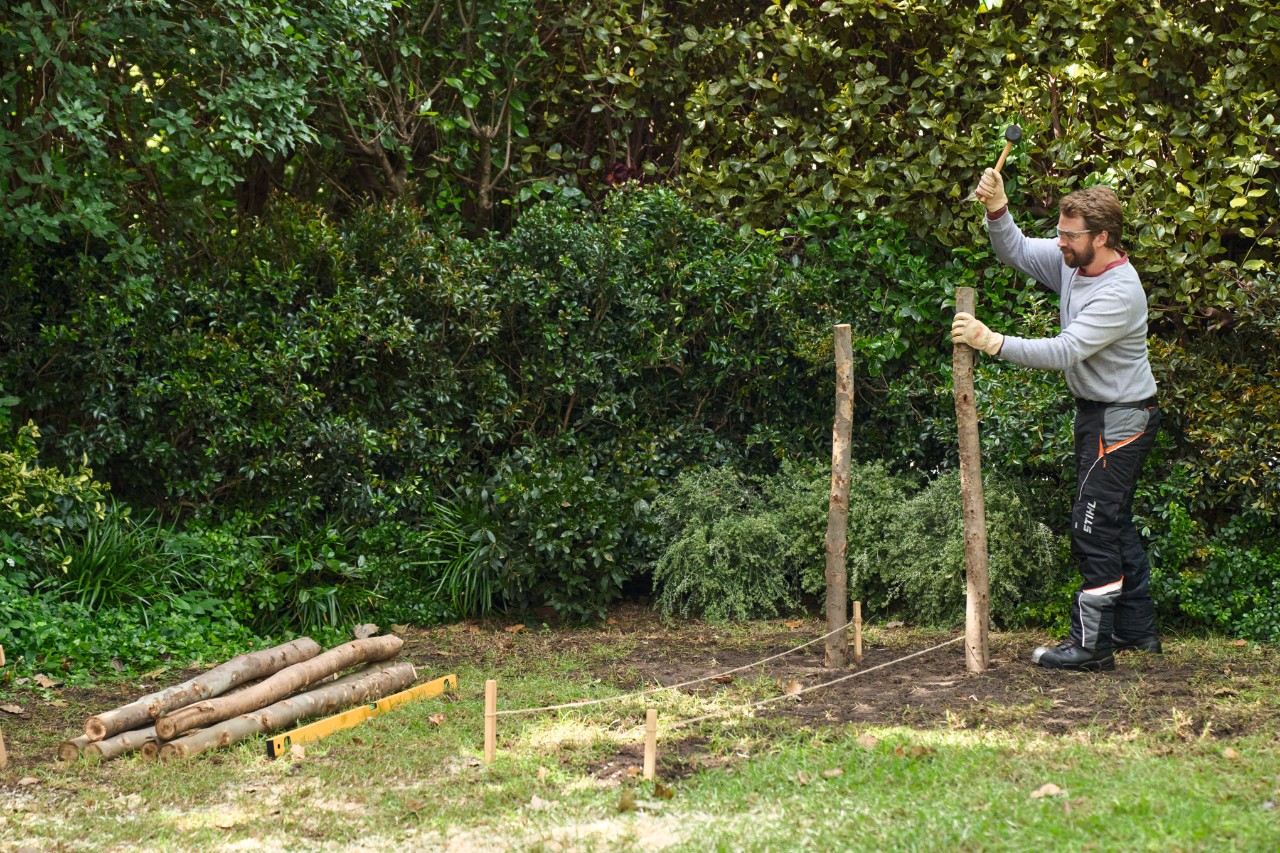 Een man slaat twee boompalen in de grond als hoekpunten voor de takkenril