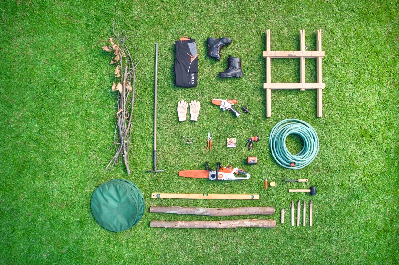 Flatlay van het nodige materiaal en gereedschap om een takkenril aan te leggen, geplaatst op een gazon