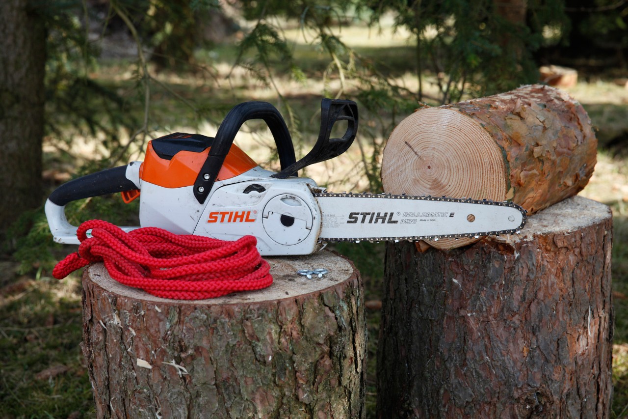 Vogelvoederhuis maken: een STIHL MSA 140 C kettingzaag zonder snoer, twee schroefogen en een rood koord op een boomstam