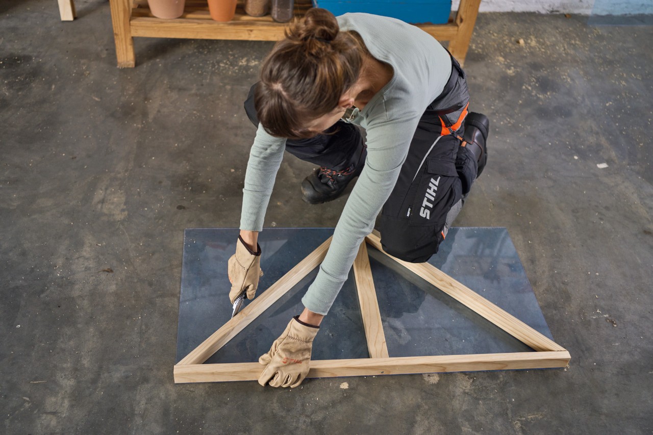 Een vrouw in een werkplaats snijdt een plexiglas plaat langs de buitenste gevelrand met een snijmes 