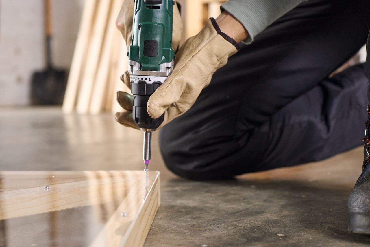 Close-up van iemand die met een accuschroevendraaier een plexiglas plaat bevestigt op hout