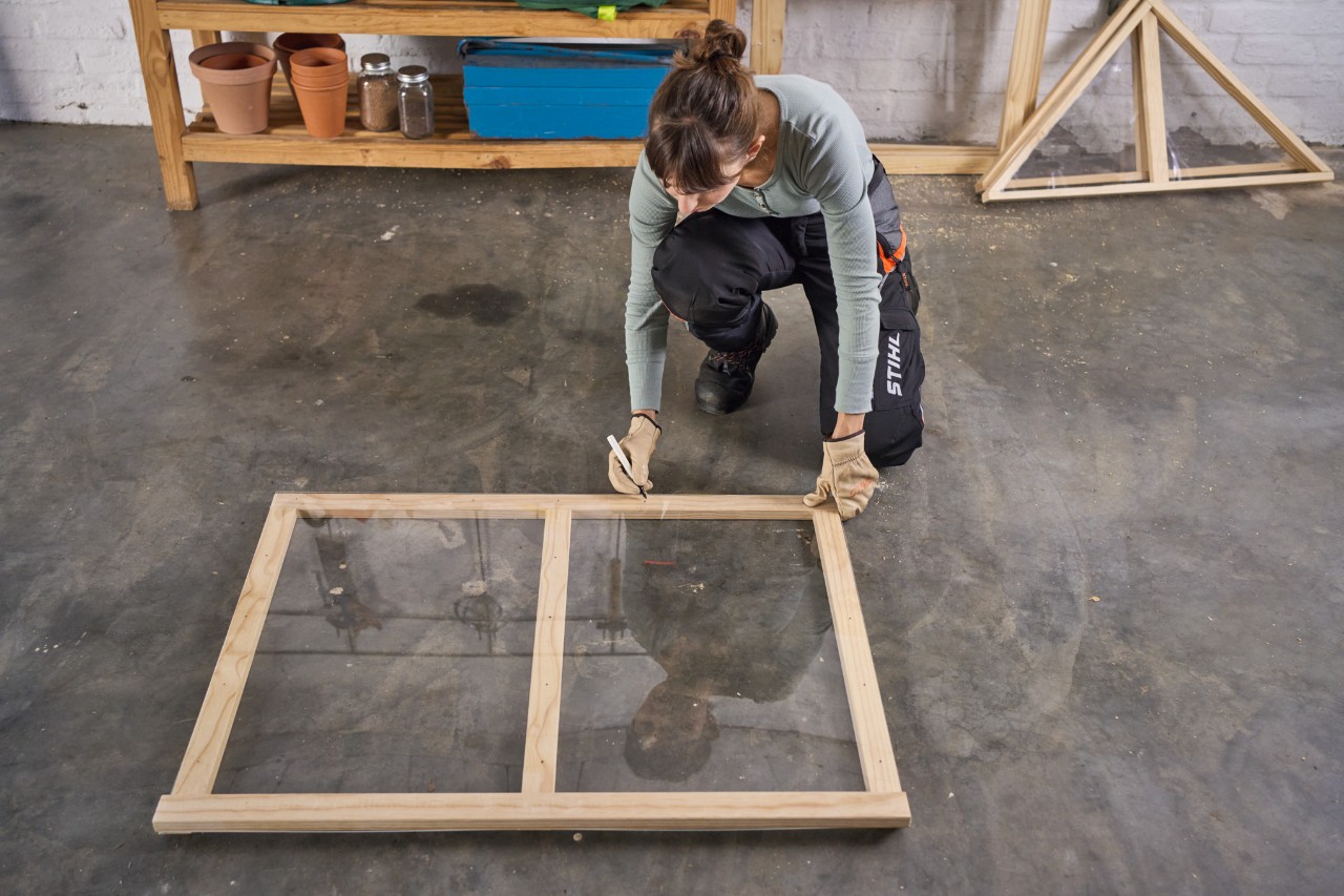 Een vrouw markeert boorgaten op een plexiglas plaat die op het raamkozijn ligt voor het verhoogde bed