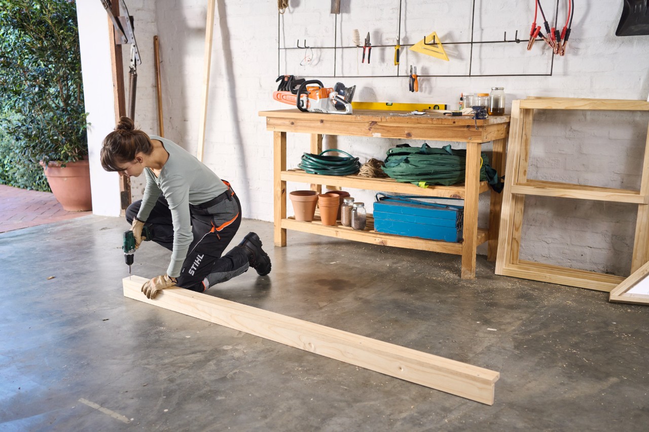 Close-up van een vrouw die in een werkplaats twee houten latten vastschroeft