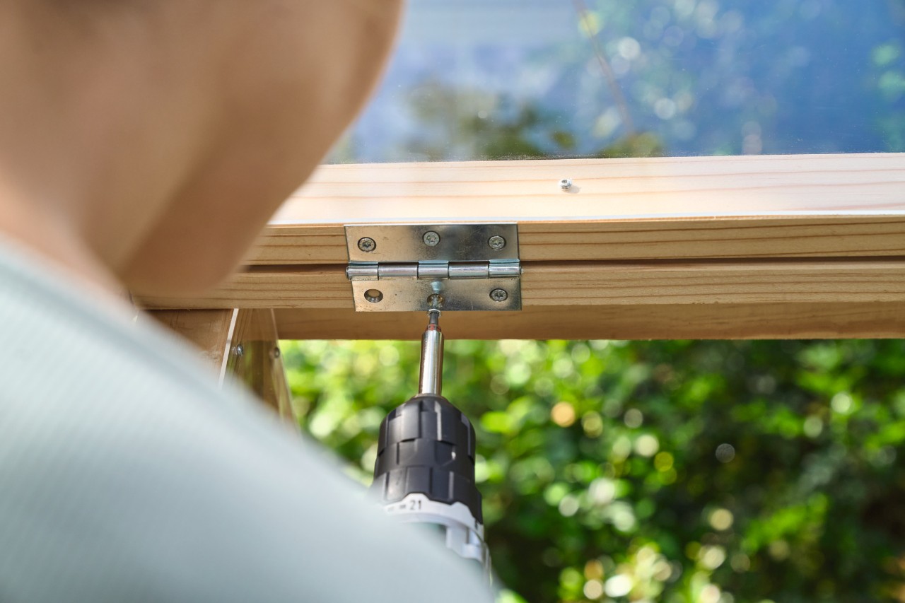 Close-up van iemand die een klapraam aan een afdekking voor een verhoogd bed schroeft