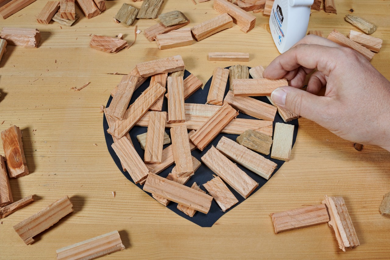 Stukken hout worden op een tafel in de vorm van een hart aan elkaar gelijmd.