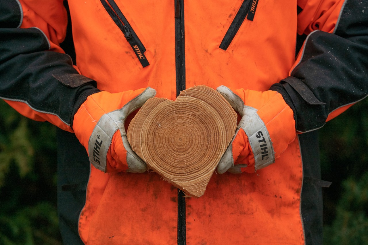 Persoon in STIHL veiligheidskledij houdt houten hart vast 