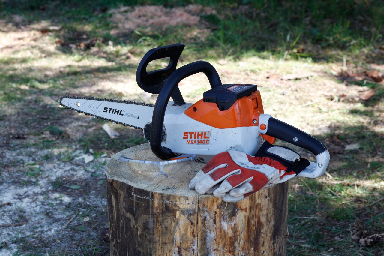 Een STIHL MSA 140 C accukettingzaag en veiligheidshandschoenen aan een boomstronk