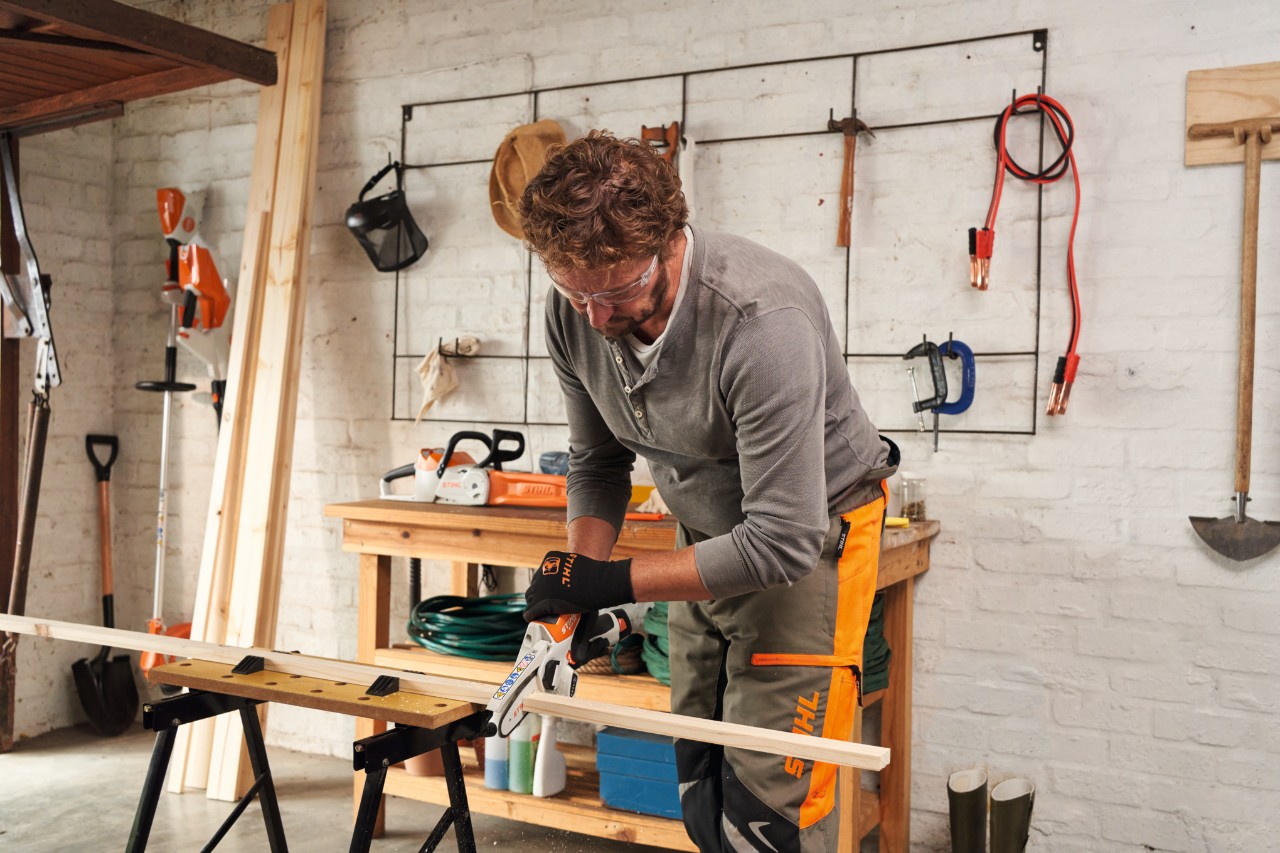Man zaagt houten planken met de STIHL GTA 26 accusnoeizaag in een werkplaats, op de achtergrond een gereedschapswand