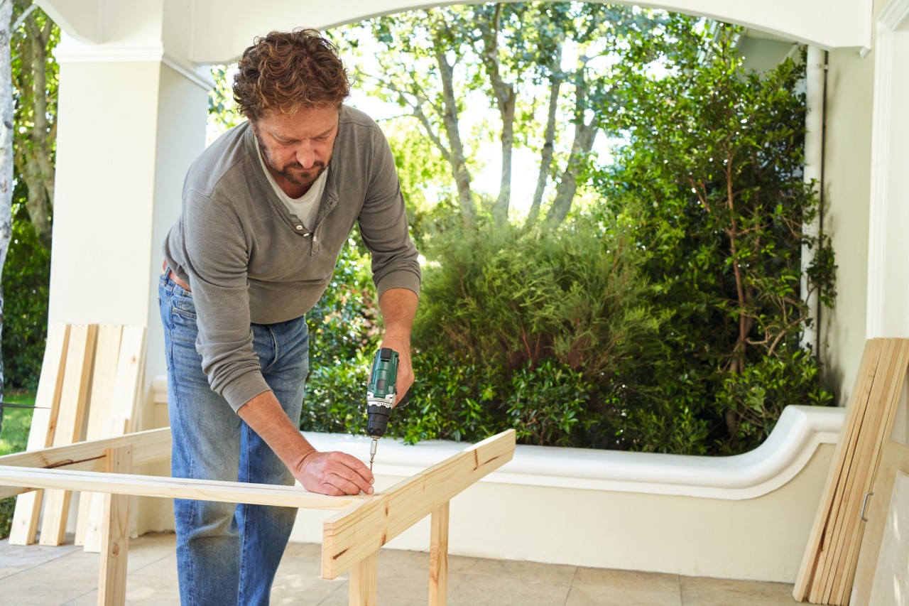 Man schroeft het frame vast voor een plantentafel op een veranda