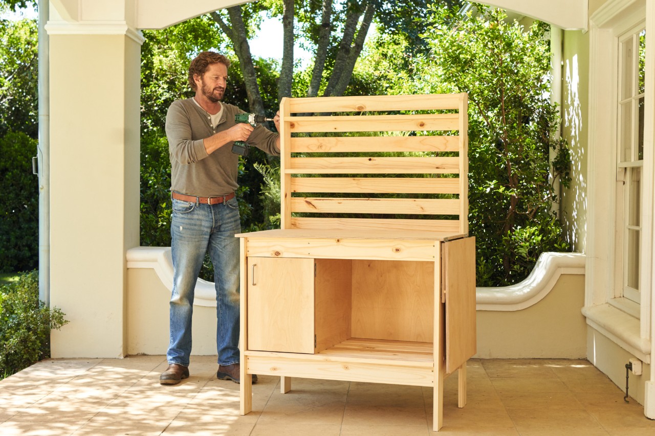 Man schroeft de planken van de bovenste achterwand van een plantentafel vast 