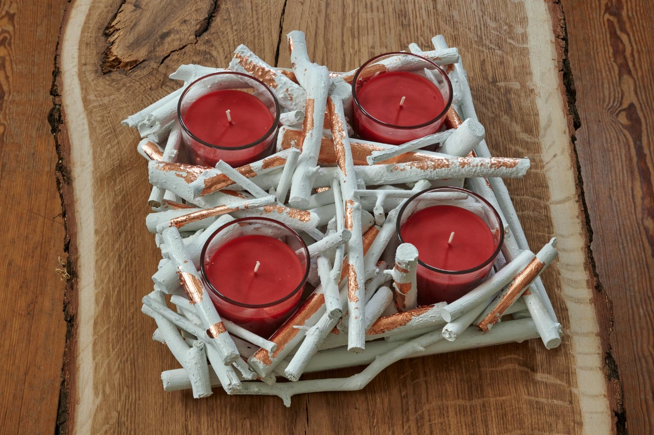 Moderne adventskrans maken: een afgewerkte krans van takjes met vier rode kaarsen in glazen