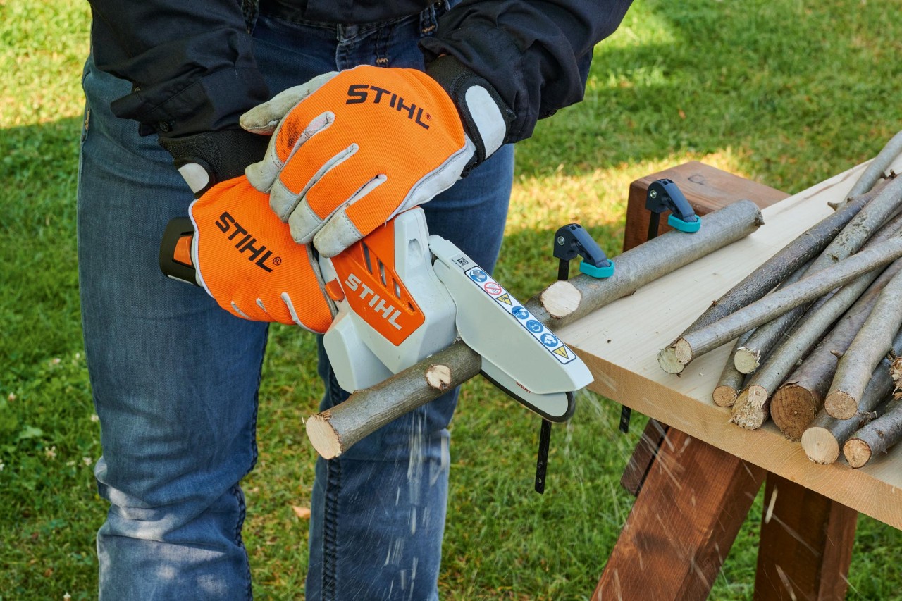 Een persoon met beschermende handschoenen zaagt takken in korte stukken met behulp van een STIHL GTA 26 snoeizaag