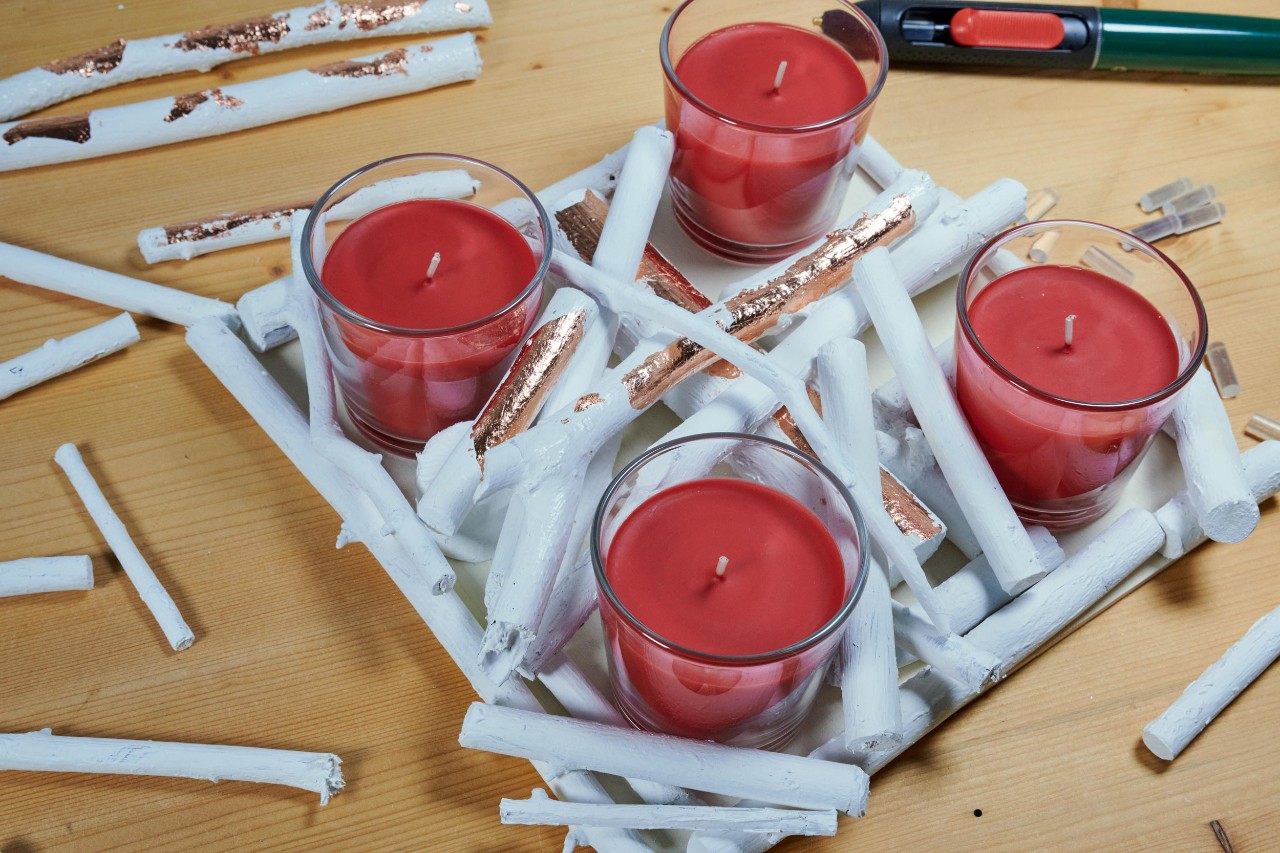 Adventskrans zelf maken: witte takjes worden rond de kaarsglazen geplaatst
