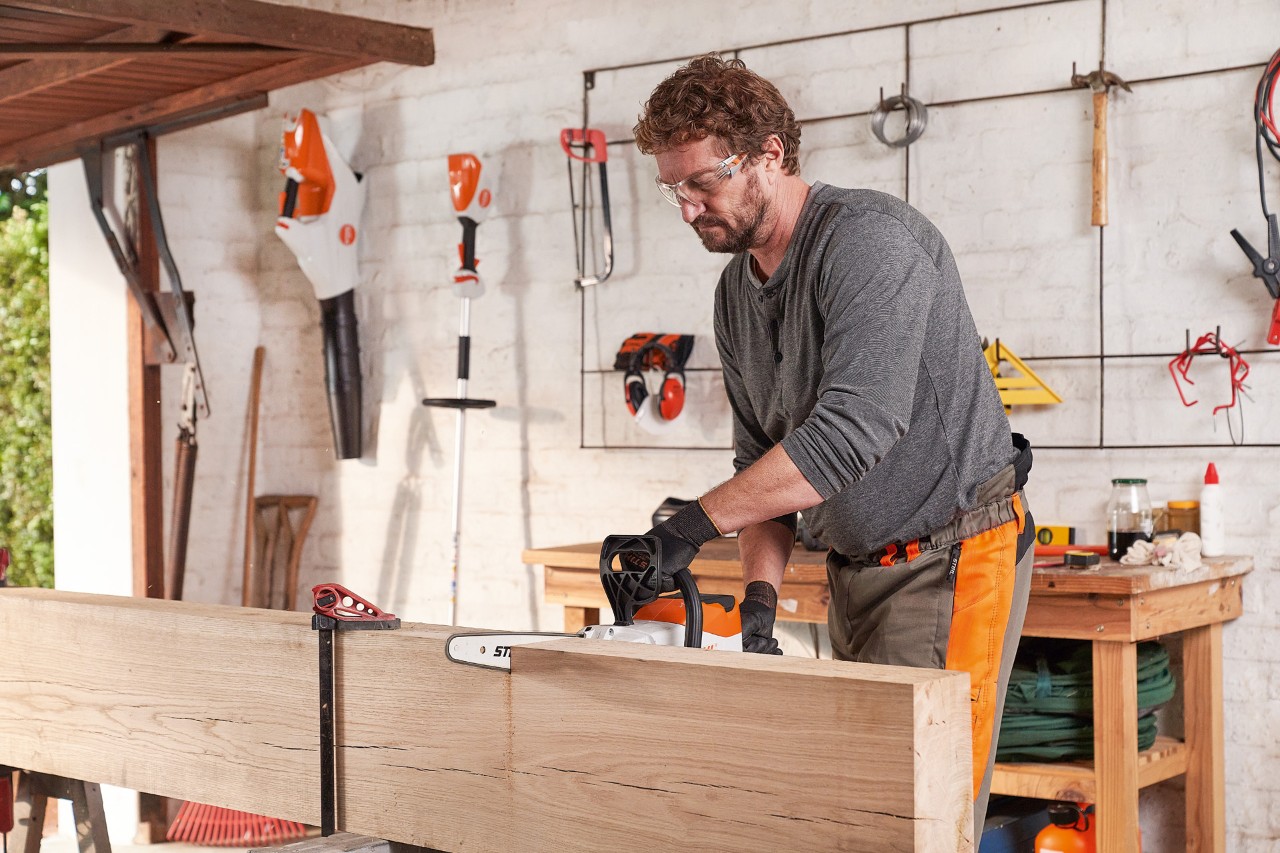 Man in veiligheidsuitrusting zaagt in werkplaats een houten plank met de STIHL MSA 140 C accumotorzaag 