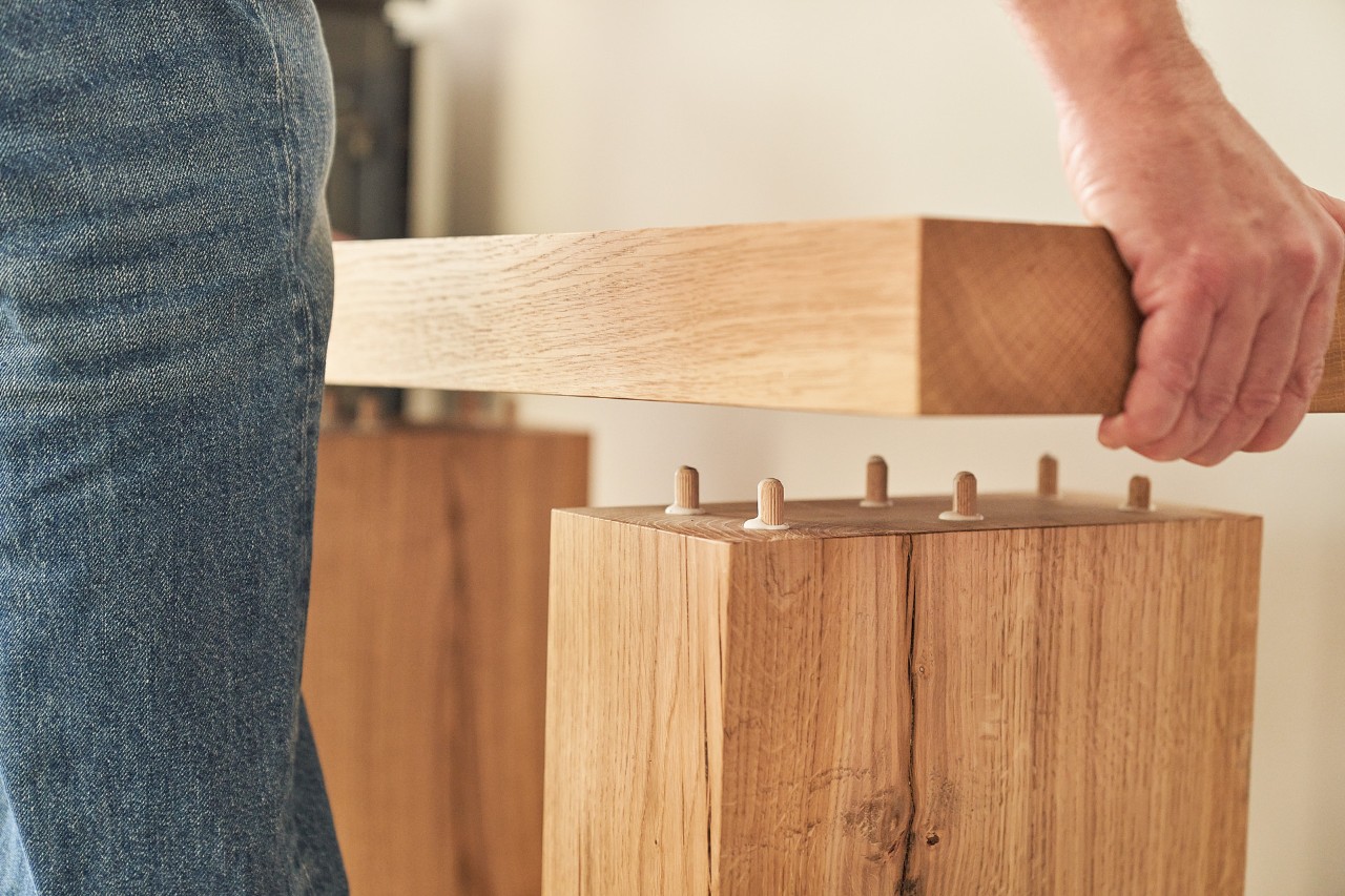 Iemand plaatst een houten plank op houten balken met behulp van deuvels 