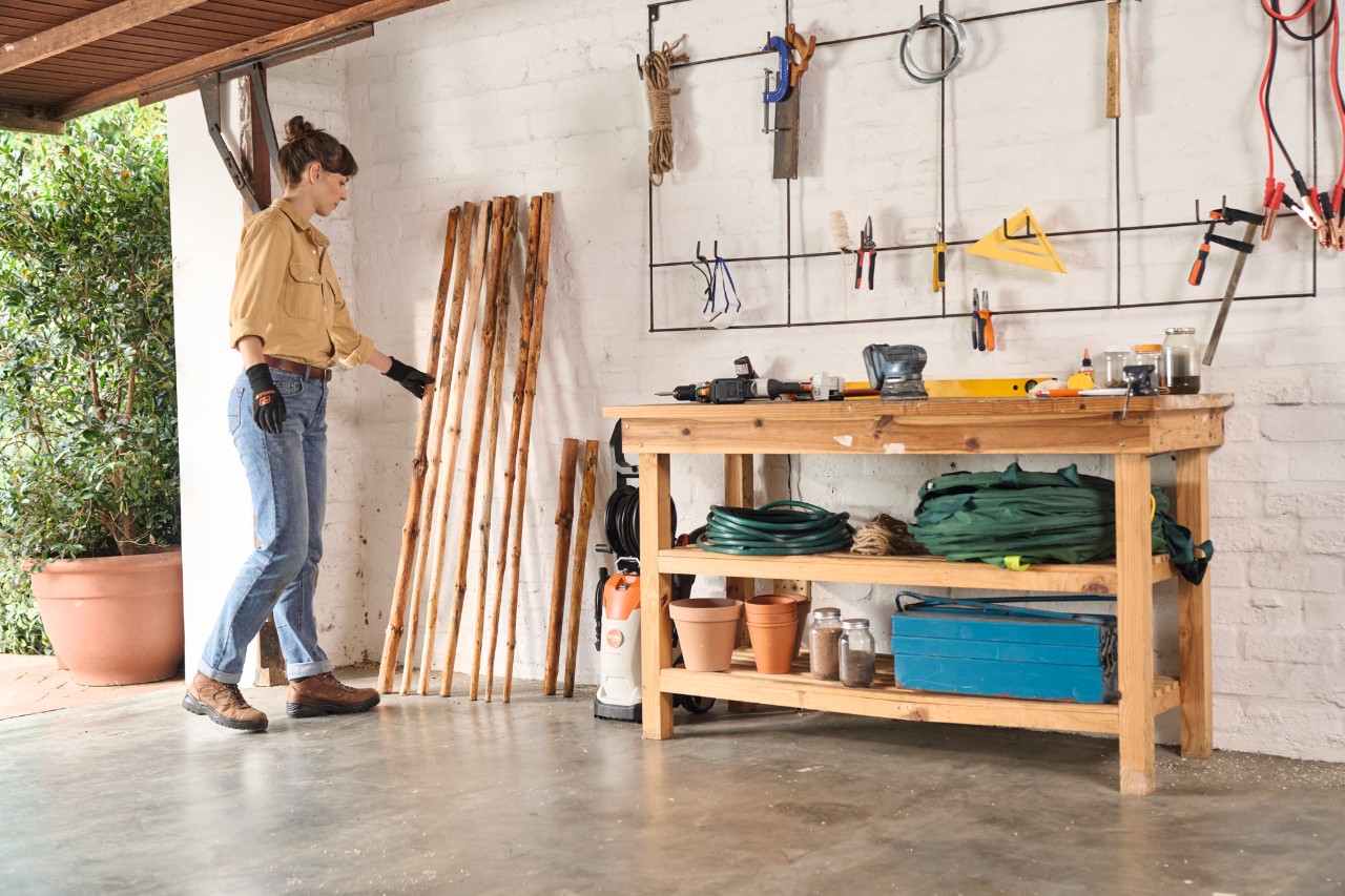 Een vrouw plaatst het hout zonder schors voor het zelfgemaakte kledingrek in de garage om te drogen