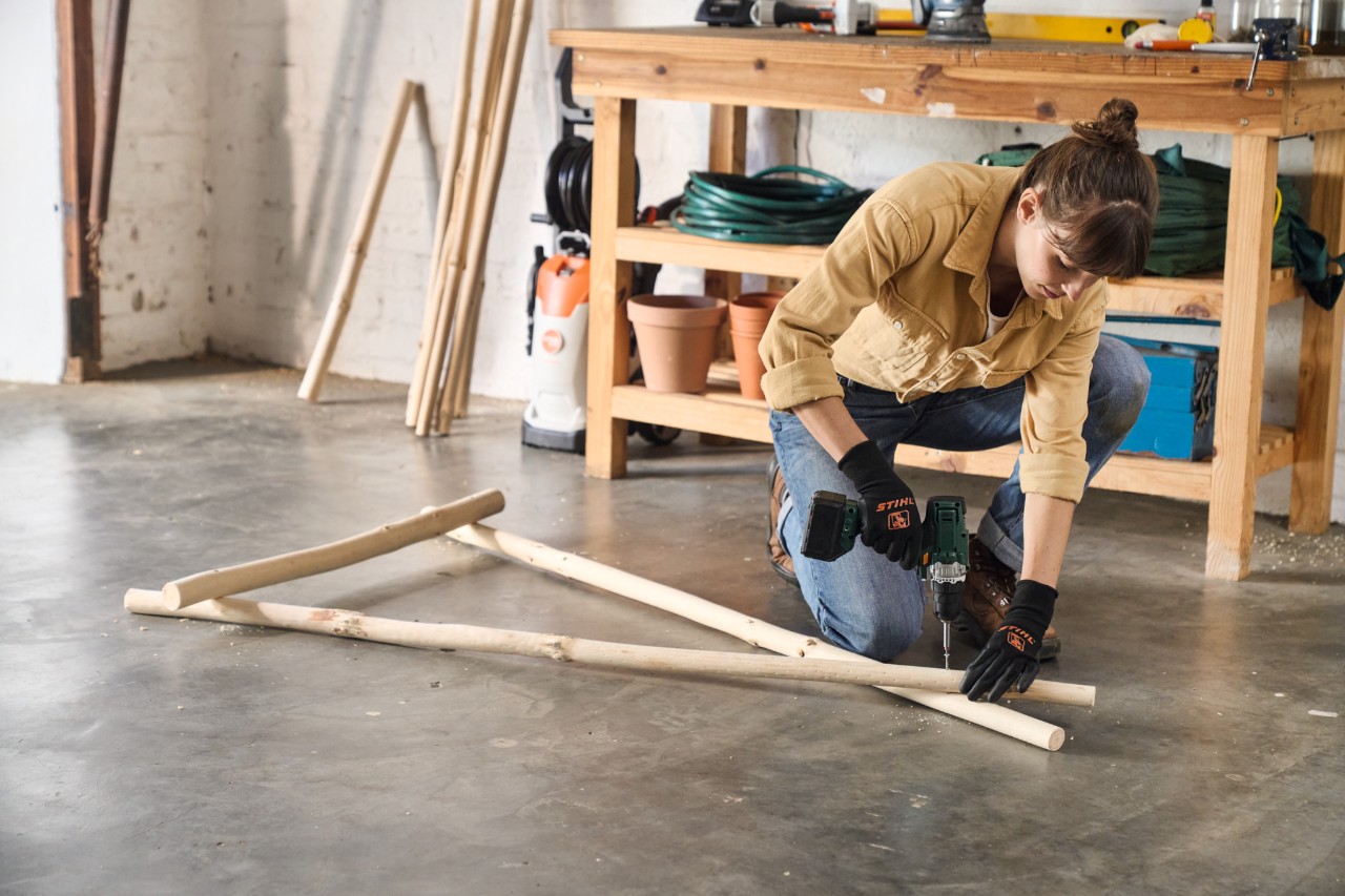 Een vrouw schroeft met een accuschroevendraaier het hout voor het zelfgemaakte kledingrek aan elkaar 