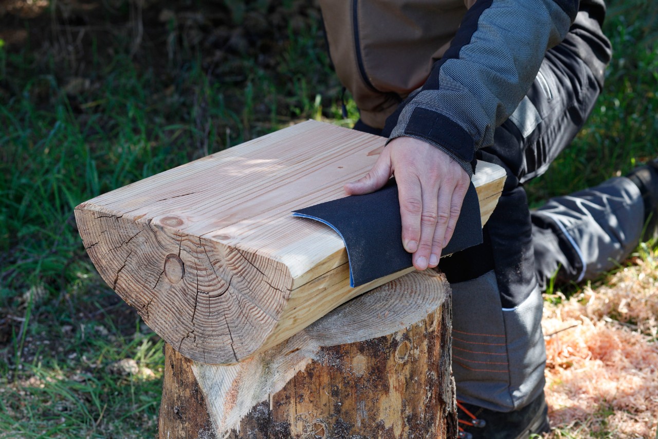 DIY-kruk van een boomstam: het gezaagde oppervlak van een gesplitst stuk hout wordt geschuurd