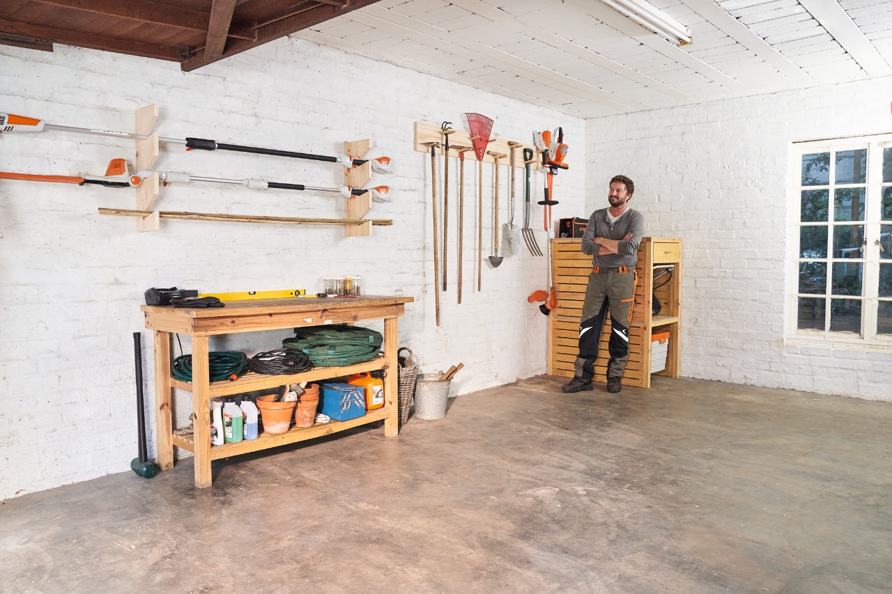 Man in een werkplaats met een rek met zelfgemaakt tuingereedschap en verschillende STIHL machines, waaronder bosmaaiers en bladblazers.