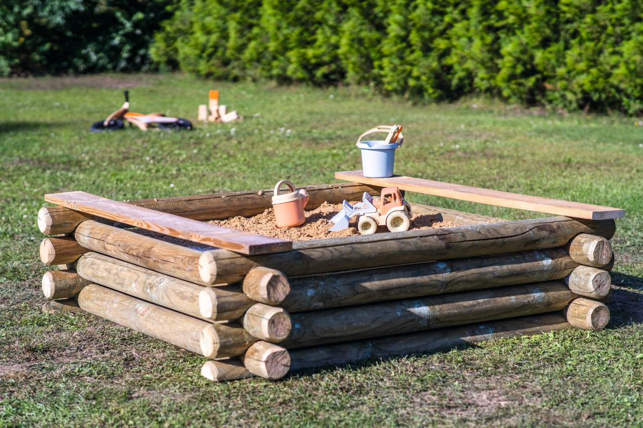 Handgemaakte zandbak met plastic speelgoed op een tuinperceel.