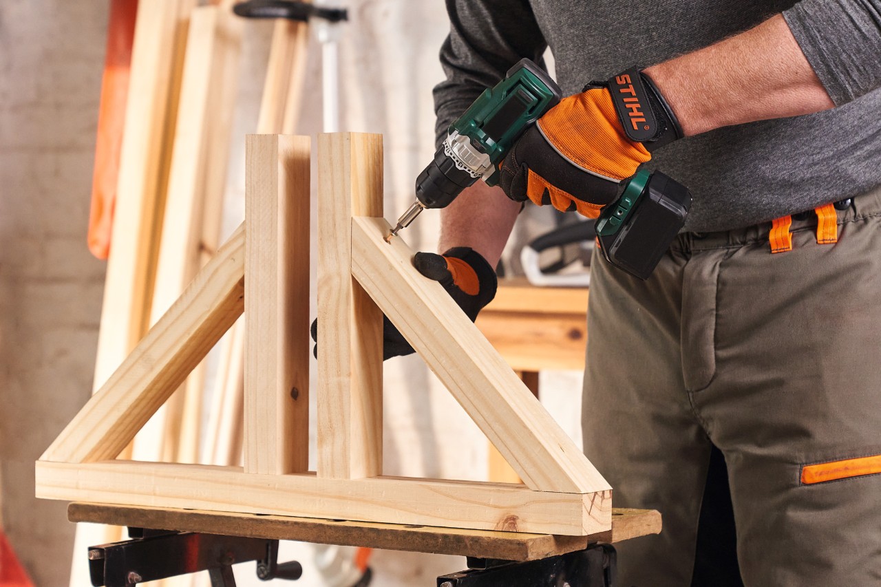 Persoon met STIHL Function Protect veiligheidshandschoenen schroeft de voetstukken in elkaar voor een houten bescherming tegen inkijk