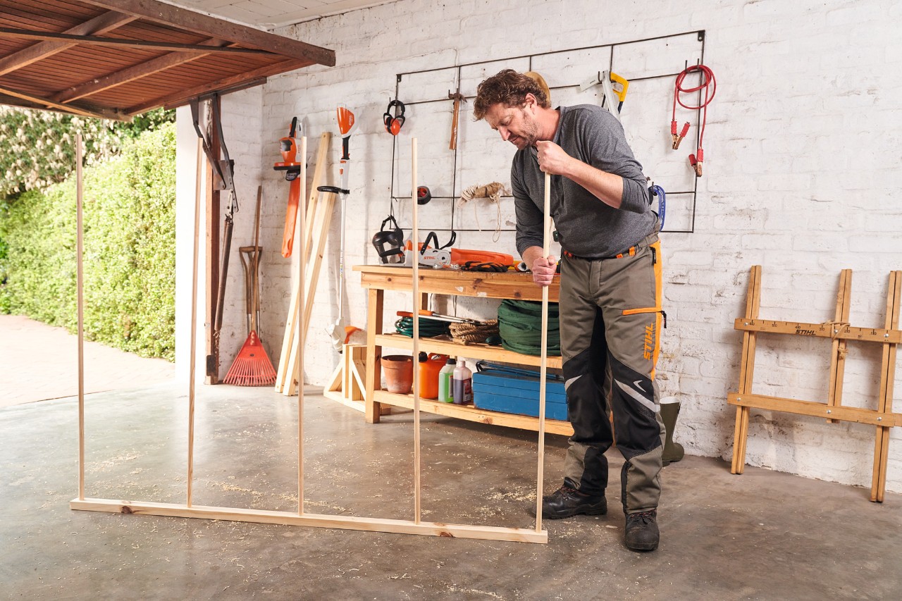 Man steekt in een garage ronde staven in elkaar voor een houten bescherming tegen inkijk