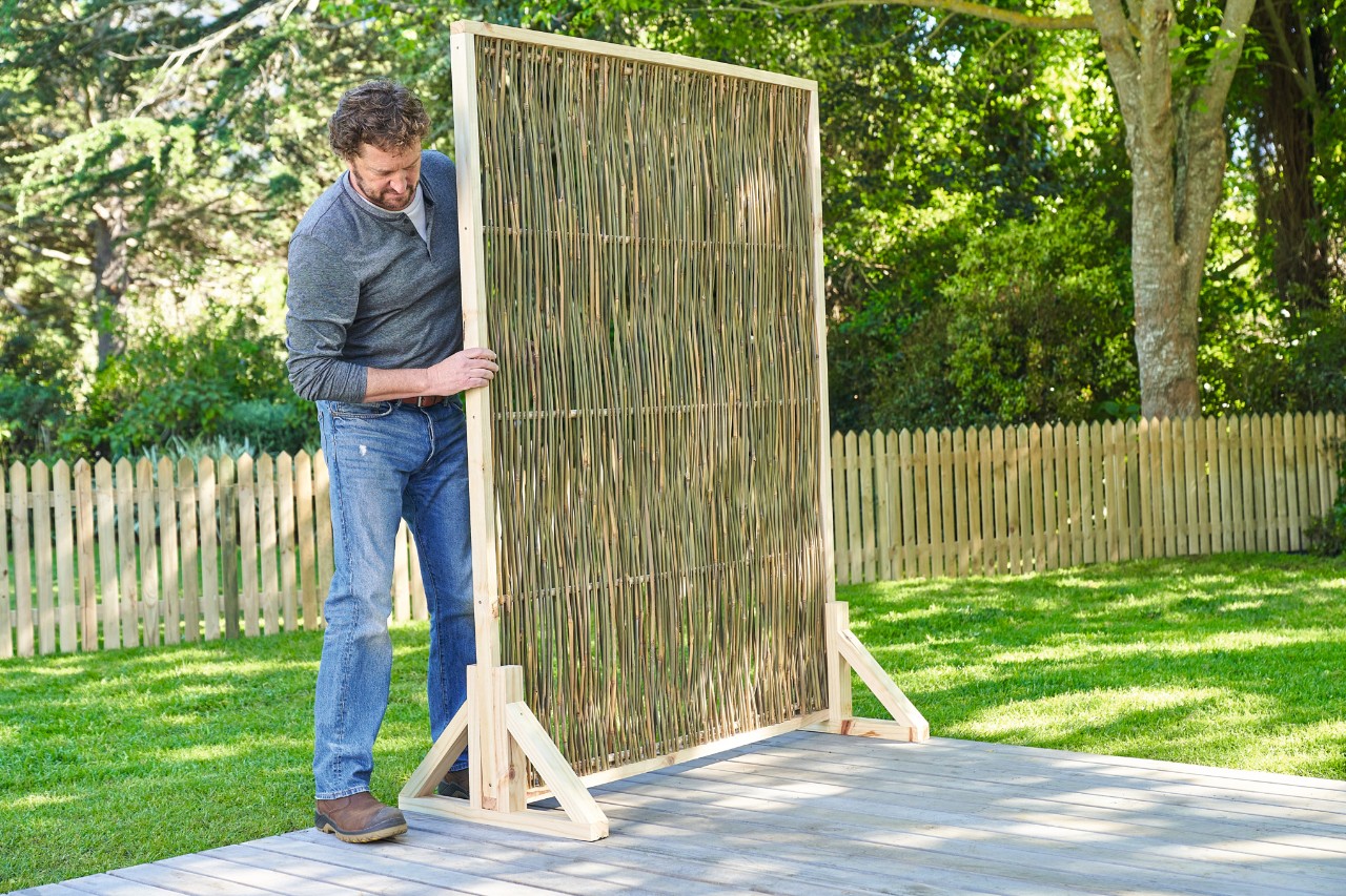 Man plaatst zijn zelfgebouwde houten schutting op de beoogde plek in de tuin
