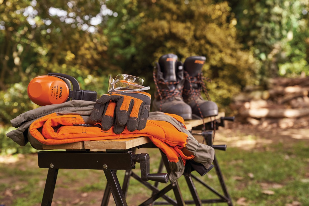 STIHL-gehoorbescherming, laarzen, veiligheidsbril en beschermende handschoenen op een werkbank in de tuin