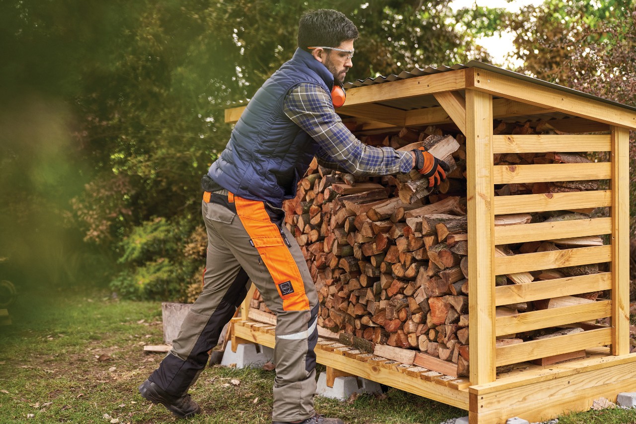 Een man stapelt brandhout in een DIY-houtopslag