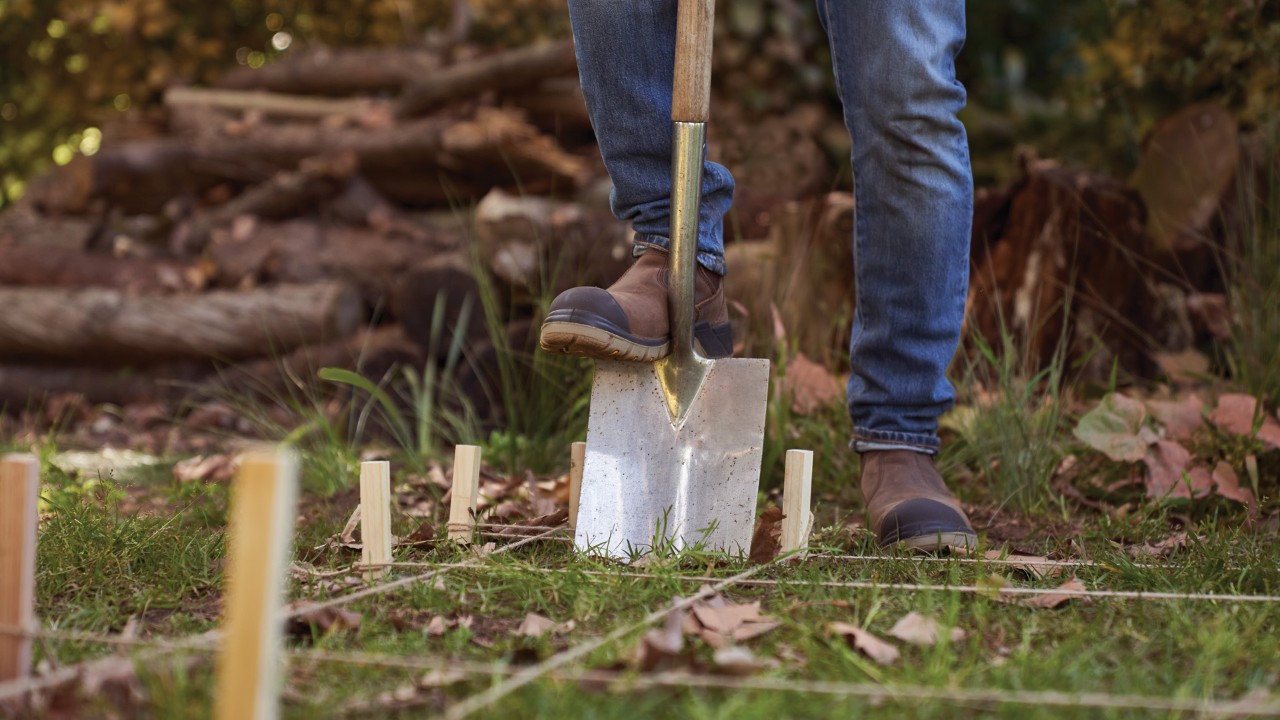 Een houthok maken: close-up van een spade die in de grond gaat op een plek die is afgebakend met paaltjes en touw