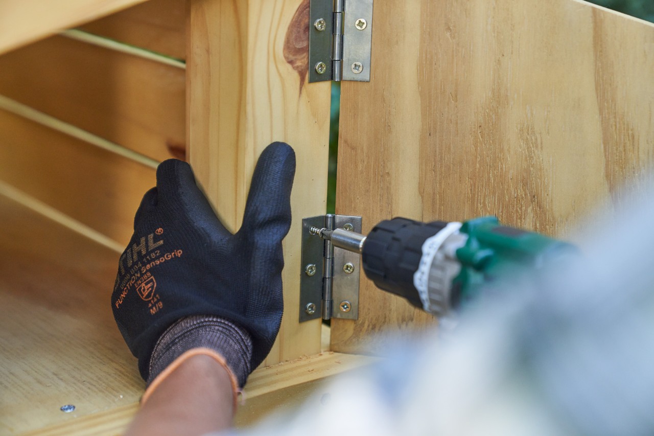 Close-up: hand met STIHL werkhandschoen FUNCTION SENSOTOUCH schroeft de deur van het opbergvak vast