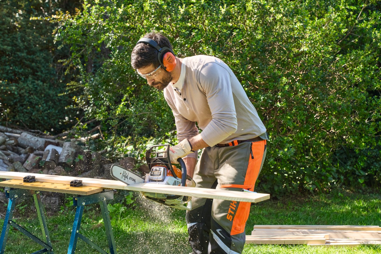 Een man aan een werkbank zaagt hout op maat