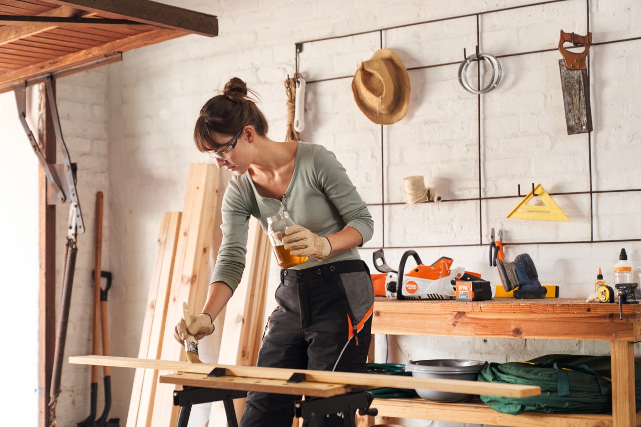 Een vrouw smeert een houten lat in met olie in een werkplaats